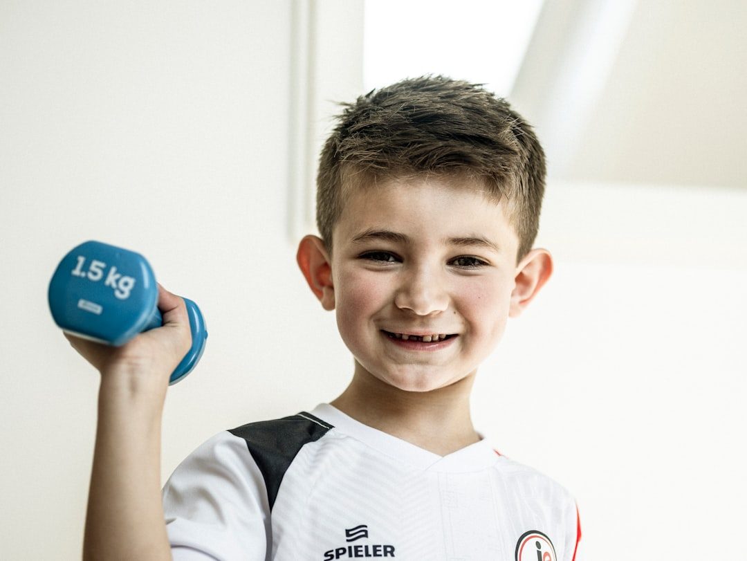 A young boy holds a dumbbell and smiles.